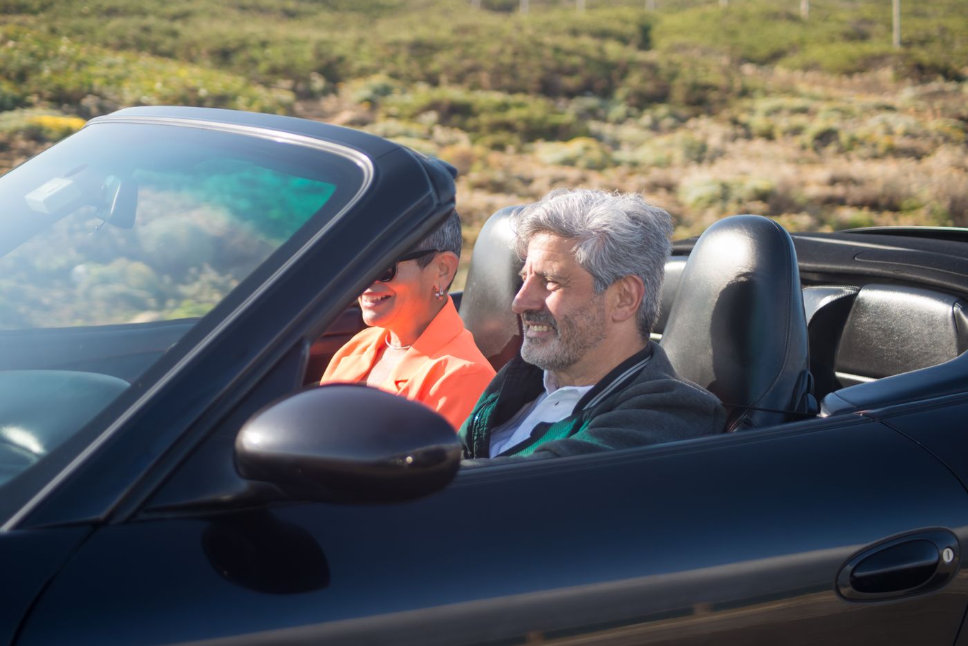A couple smiling at each other in an open-top car